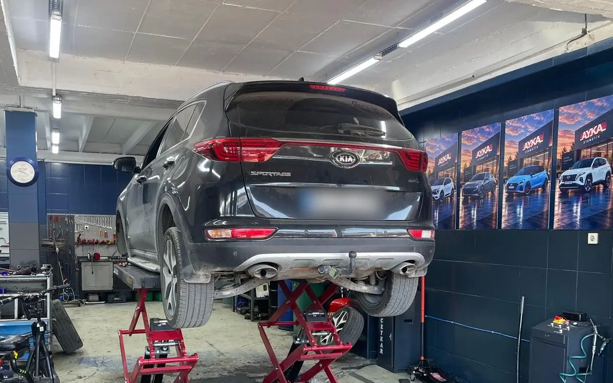 Ayka Otomotiv atölyesi: makaslı lift üzerinde Kia Sportage, mavi duvarda AYKA afişleri