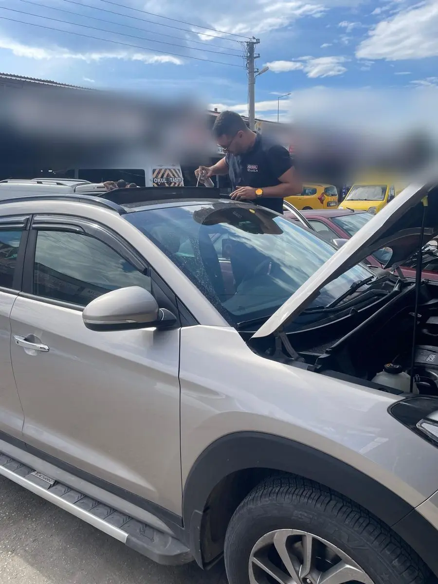 Atölye önünde kaputu açık Hyundai Tucson'un tavanında çalışan AYKA tişörtlü usta