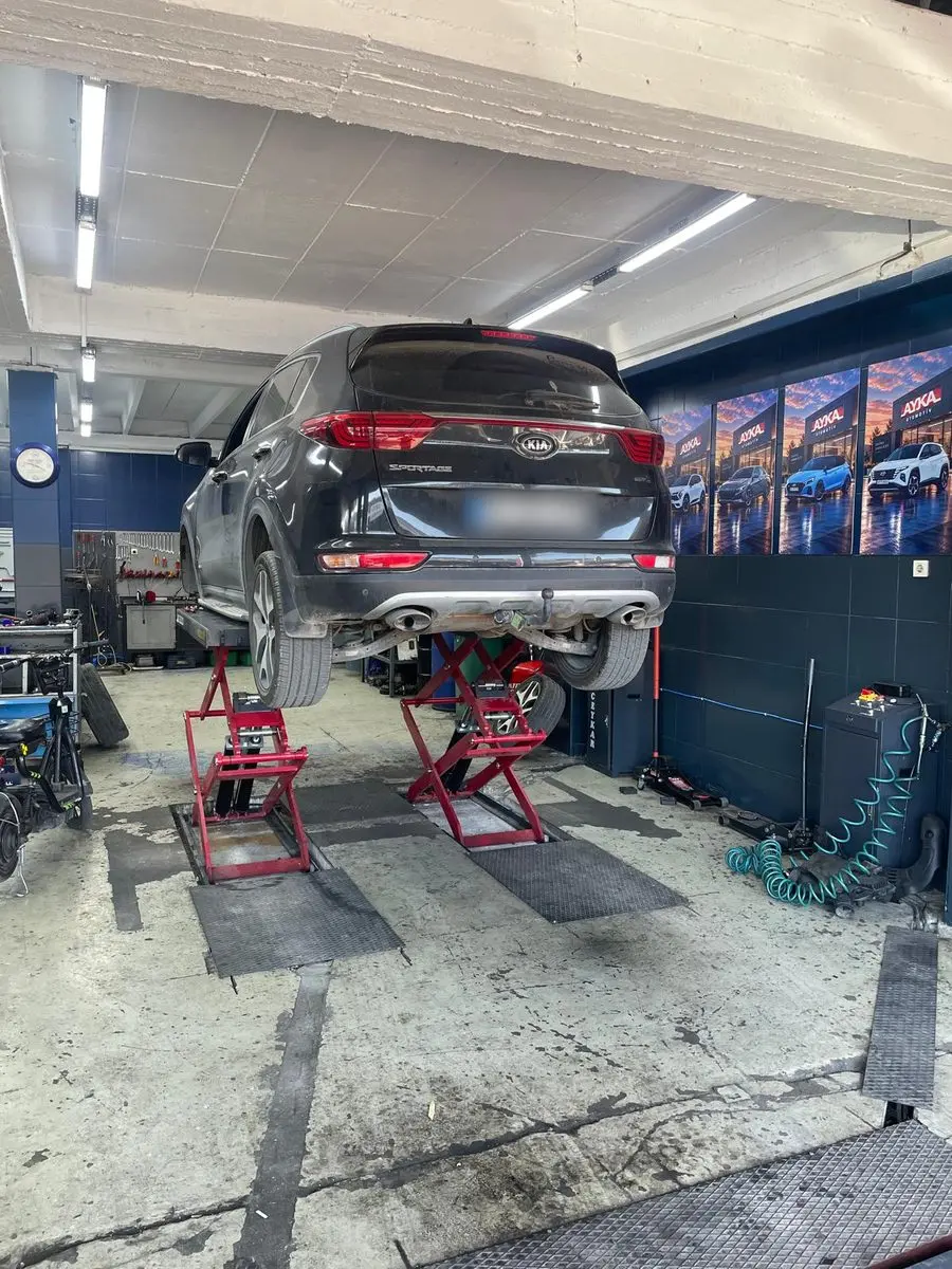 Ayka Otomotiv atölyesinde makaslı lift üzerinde kaldırılmış siyah Kia Sportage, duvarda AYKA afişleri