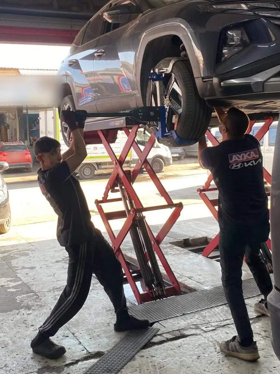 Makaslı lift üzerinde kaldırılmış Hyundai'nin altında çalışan iki AYKA ustası