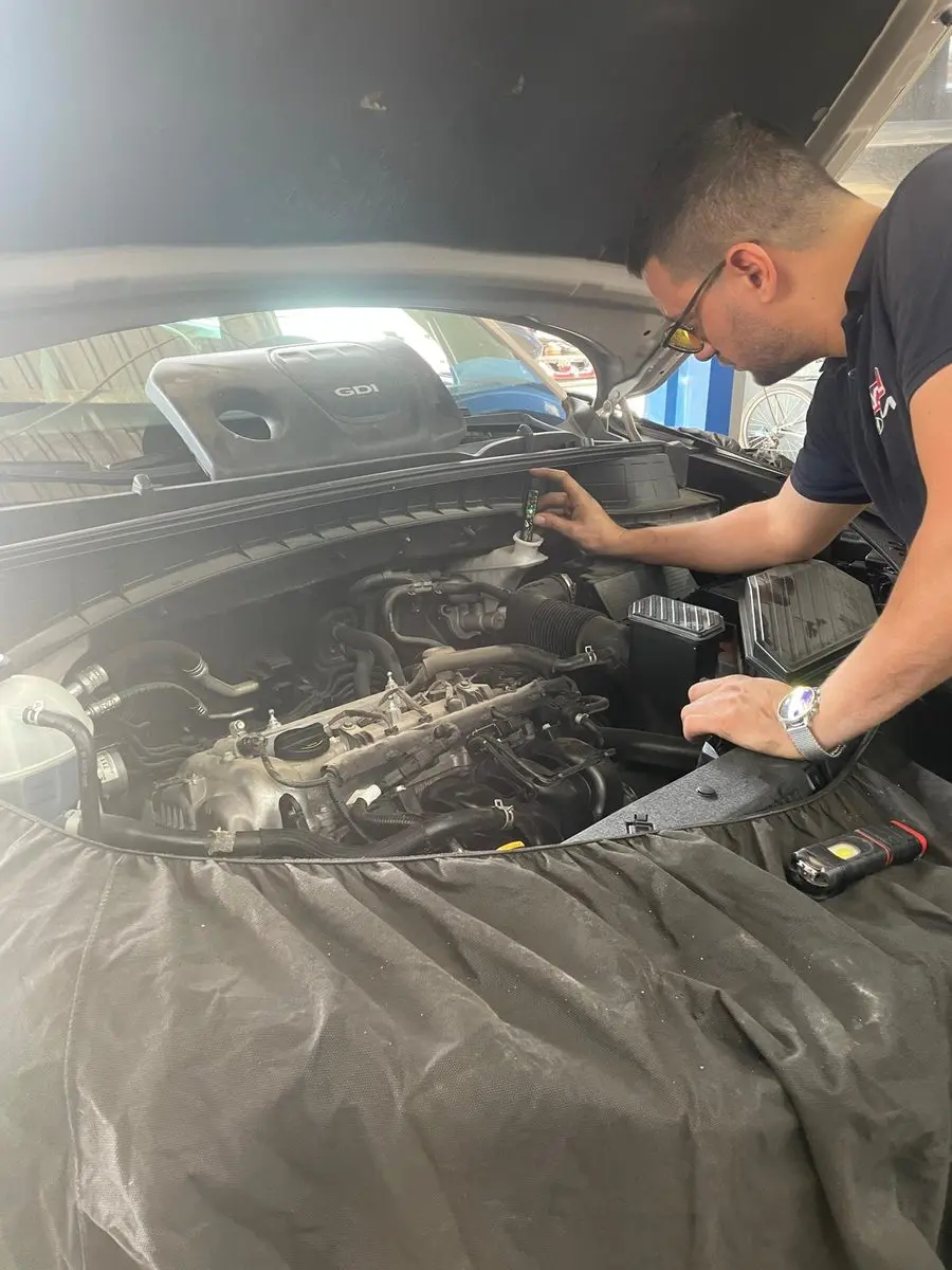 Çamurluğu örtüyle korunan GDi motorlu aracın motor bölmesinde ölçüm cihazıyla sıvı kontrolü yapan usta
