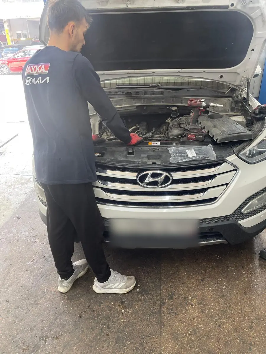 Kaputu açık beyaz Hyundai Santa Fe'nin motor bölmesinde çalışan AYKA tişörtlü usta