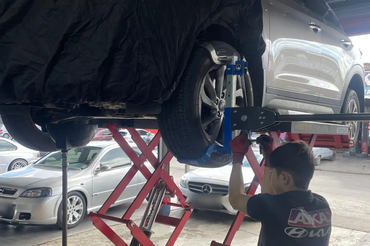Makaslı lift üzerinde kaldırılmış aracın tekerlek ve alt takımında çalışan usta